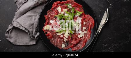 Hors-d'œuvre de viande froide carpaccio de bœuf avec parmesan et arugula sur une assiette noire Banque D'Images