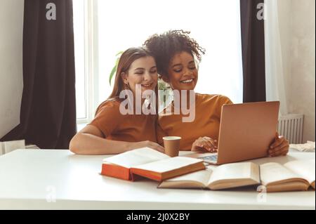 Deux amies heureuses assises devant un ordinateur portable, préparant les examens ensemble à la maison Banque D'Images