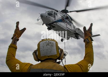 MER DES PHILIPPINES (19 mars 2022) Aviation Boatswain’s Mate 2nd Class Alasdair Reid, de Wellington (Nouvelle-Zélande), signale un Super Puma AS332 sur le pont de vol du porte-avions de la classe Nimitz USS Abraham Lincoln (CVN 72) Au cours d'un réapprovisionnement vertical en mer avec le navire de fret et de munitions du Commandement du Seallift militaire USNS Matthew Perry (T-AKE 9). Abraham Lincoln Strike Group est en cours de déploiement prévu dans la zone d'exploitation de la flotte américaine 7th afin d'améliorer l'interopérabilité par le biais d'alliances et de partenariats tout en servant de force de réaction prête à l'emploi pour soutenir un Indo-Paci libre et ouvert Banque D'Images