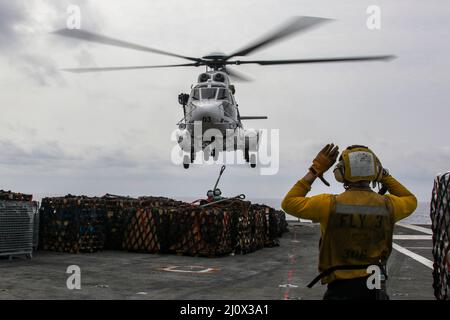 MER DES PHILIPPINES (19 mars 2022) Aviation Boatswain’s Mate 2nd Class Alasdair Reid, de Wellington (Nouvelle-Zélande), signale un Super Puma AS332 sur le pont de vol du porte-avions de la classe Nimitz USS Abraham Lincoln (CVN 72) Au cours d'un réapprovisionnement vertical en mer avec le navire de fret et de munitions du Commandement du Seallift militaire USNS Matthew Perry (T-AKE 9). Abraham Lincoln Strike Group est en cours de déploiement prévu dans la zone d'exploitation de la flotte américaine 7th afin d'améliorer l'interopérabilité par le biais d'alliances et de partenariats tout en servant de force de réaction prête à l'emploi pour soutenir un Indo-Paci libre et ouvert Banque D'Images