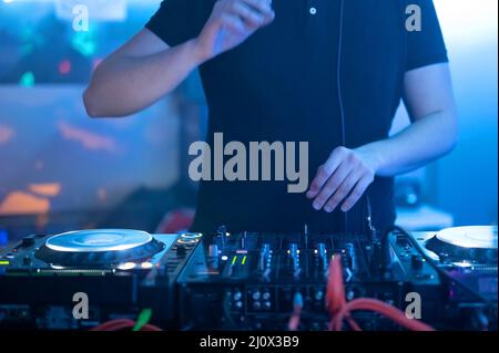 Gros plan vue de face des mains du DJ contrôlant une table de musique dans une discothèque. Banque D'Images