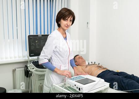 Le médecin cardiologue effectue une procédure d'électrocardiographie sur un homme allongé sur un lit à l'hôpital. Test ECG d'un homme dans une clinique moderne. Banque D'Images
