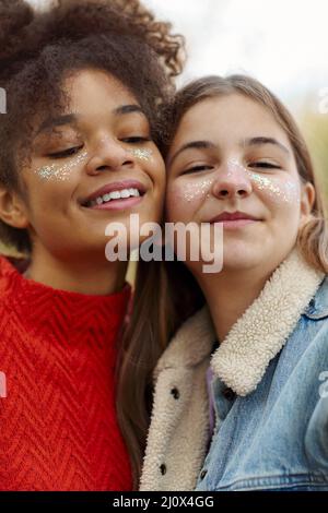 Portrait de deux amies multiraciales heureuses souriant à l'appareil photo tout en passant du temps dans la nature de l'automne, des filles gaies d'adolescents de diffuse Banque D'Images