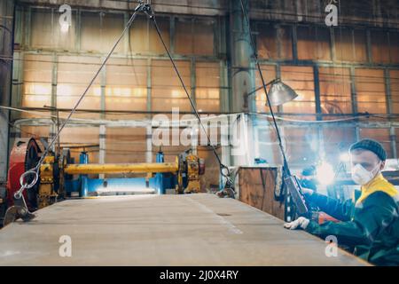 L'employé lève la tôle à l'aide d'un palan à chaîne de grue avec télécommande et crochet à l'usine industrielle. Banque D'Images