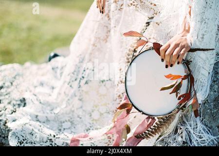 Tambourin décoré de plumes et de rubans dans la main d'une femme dans une robe Banque D'Images