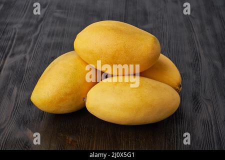 Quatre mangues de fruits entières sur une table en bois. Grands fruits jaunes mûrs et juteux Banque D'Images