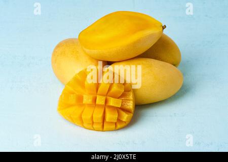 Quatre fruits de mangue entiers sur une table bleu vif et coupés en tranches. Gros fruits jaunes juteux Banque D'Images