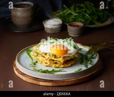 Gaufres à la pomme de terre avec œufs frits, roquette et sauce avocat. Copieux petit déjeuner copieux. Table marron foncé. Banque D'Images