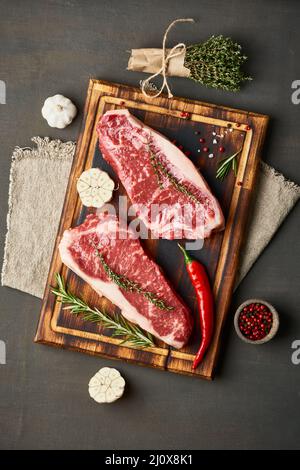 Gros morceau entier de viande de bœuf crue. Assaisonner le steak avec du sel, du thym, de l'ail. Verticale Banque D'Images