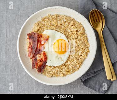 Flocons d'avoine, œufs frits et bacon frit. Copieux petit déjeuner riche en calories, source d'énergie. Banque D'Images