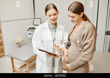 Portrait de jeune femme médecin consultant une femme enceinte en clinique et utilisant une tablette numérique Banque D'Images