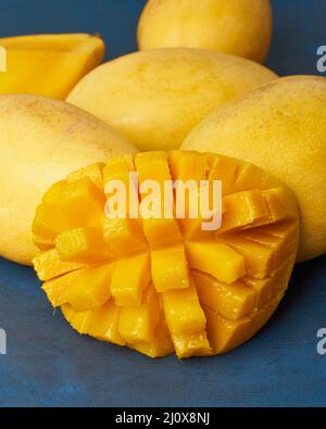 Quatre fruits de mangue entiers sur une table bleu foncé et coupés en tranches. Gros fruits jaunes mûrs juteux Banque D'Images