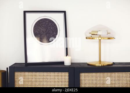 Commode en bois noir avec affiche carte encadrée d'étoiles, lampe et bougie dans un intérieur minimaliste Banque D'Images