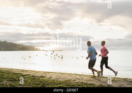 Vue latérale sur la plage de jogging des couples aînés Banque D'Images