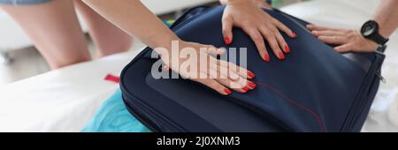 Homme et femme essayant de fermer la valise complète avec des choses de gros plan Banque D'Images