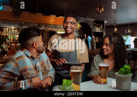 Serveur afro-américain servant couple et amis au restaurant Banque D'Images