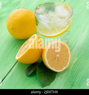 Limonade dans un verre, moitié citron, feuilles fraîches sur la table verte. Une boisson fraîche rafraîchissante d'eau avec de la glace, de la menthe et des tranches o Banque D'Images