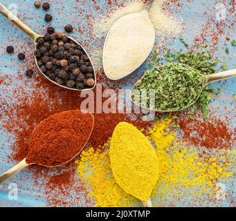 Épices fraisées - ail, curcuma, paprika, origan. Ronde de cuillères dorées sur une table en bois bleu. Vue de dessus, gros plan Banque D'Images