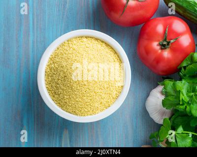 Plats végétariens - blé, grain de couscous cru dans un bol blanc sur fond de bois bleu, légumes frais - persil, concombre Banque D'Images