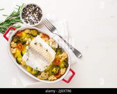 Morue de poisson cuite au four avec des légumes - alimentation saine alimentation saine. Arrière-plan en bois blanc clair, espace de copie, vue de dessus. Banque D'Images