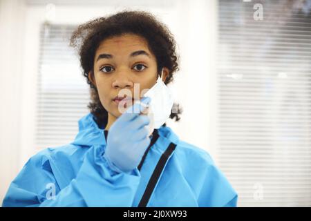 Femme américaine fatiguée frustrée travailleur médical africain dans l'équipement de protection enlever le masque facial Banque D'Images