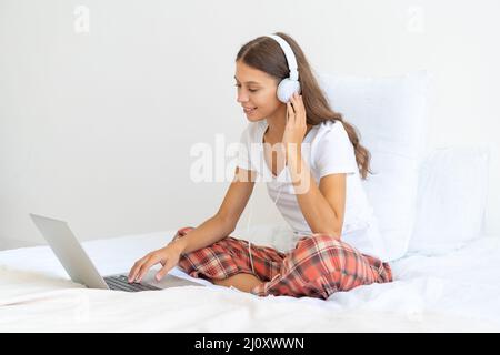 Jeune femme dans un casque étudiant en ligne, travaillant à la maison à l'aide d'un ordinateur portable Banque D'Images