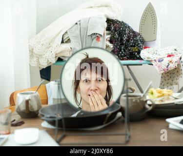 Concept de ménage abandonné. La femme se regarde dans le miroir sur fond de désordre Banque D'Images