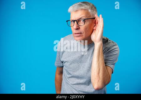 Homme d'âge moyen sur fond iblue avec écoute de la main sur l'oreille Banque D'Images