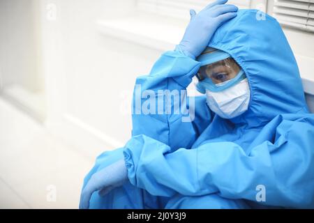 Infirmière déprimée dans l'équipement de protection individuelle EPI après un quart difficile pendant Covid-19 Banque D'Images