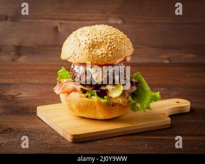 Gros délicieux hamburger maison avec côtelettes de bœuf, fromage, oignon, tomate et laitue sur des petits pains grillés. Restauration rapide américaine, santé Banque D'Images