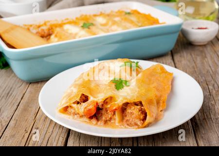 Cannelloni avec remplissage de bœuf haché, tomates, cuites avec sauce tomate bechamel, vue latérale, vieux fond en bois sombre Banque D'Images