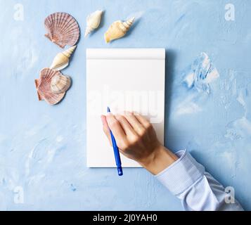 Femme écrit dans le carnet sur la table bleu de pierre, maquette avec cadre de bord de mer, vue de dessus, planification de vacances par mer Banque D'Images