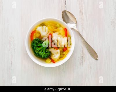 Soupe végétarienne aux légumes de printemps avec chou-fleur, brocoli, poivre, carotte, pois verts, persil. Vue de dessus, blanc Banque D'Images