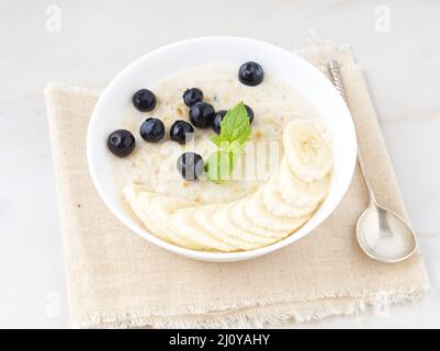 Grand bol de flocons d'avoine savoureux et sains avec fruits et baies pour le petit déjeuner, repas du matin. Vue latérale, table en marbre blanc Banque D'Images