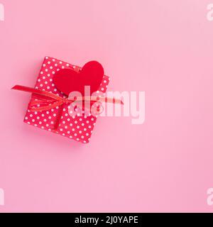 Cadeau dans boîte cadeau rouge avec noeud, coeur rouge, fond rose, vue de dessus, espace vide pour le texte. Banque D'Images