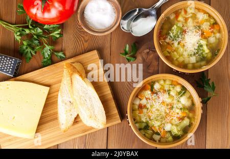 Deux bols de soupe minestrone avec fromage sur planche à découper, légumes sur fond de bois rustique, vue de dessus, grande largeur. Banque D'Images