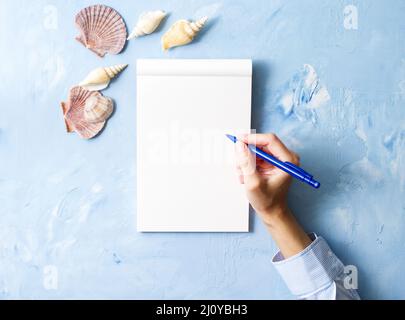 Femme écrit dans un carnet sur une table bleue en pierre, maquette avec cadre de bord de mer, vue de dessus Banque D'Images