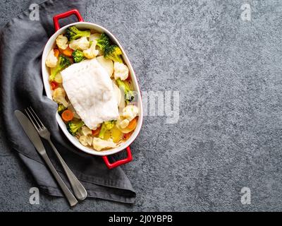 Morue de poisson cuite au four avec des légumes - alimentation saine alimentation saine. Arrière-plan en pierre grise, espace de copie, vue de dessus Banque D'Images