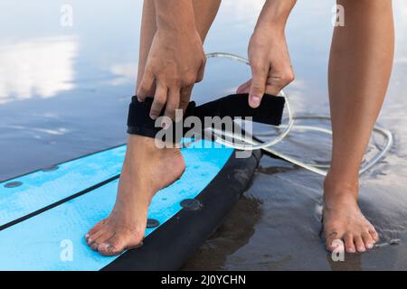 Une femme attache la laisse de surf sur sa cheville Banque D'Images