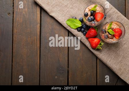 Mousse au chocolat aux fruits à baies, noix enrobées et feuilles de menthe servies dans des verres en toile de jute à la table Banque D'Images