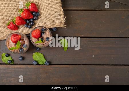 Mousse au chocolat aux fruits rouges, noix enrobées et feuilles de menthe servies dans des verres en toile de jute sur la table Banque D'Images