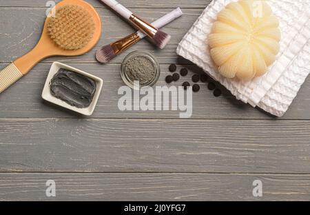 Bols de masque facial à charbon actif, poudre, fournitures de bain et pinceaux de maquillage sur fond de bois gris Banque D'Images