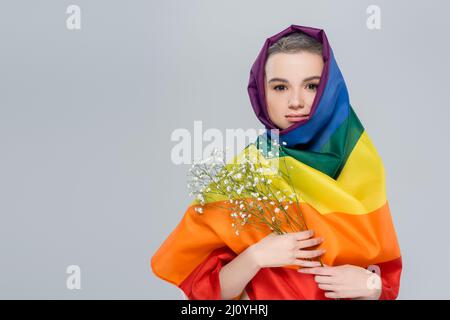 jeune femme enveloppée dans un drapeau lgbt tenant des fleurs de gitsophila isolées sur le gris Banque D'Images