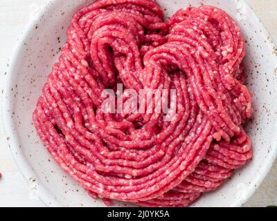 Hachez le bœuf, la viande hachée avec des ingrédients pour cuisiner sur une table rustique en bois blanc Banque D'Images