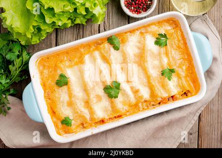 Cannelloni avec remplissage de boeuf haché, tomates, cuit avec sauce tomate bechamel, vue sur le dessus, vieux fond en bois sombre Banque D'Images