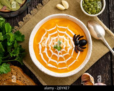 Nourriture drôle pour Halloween. Soupe de purée de citrouille, toile d'araignée, table en bois sombre, vue sur le dessus. Banque D'Images