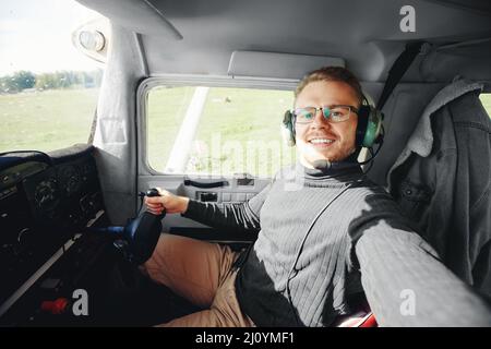 Selfie photo Happy MAN pilote dans un cockpit d'avion léger, casque aviateur et volant. Banque D'Images