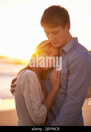 Un moment dans mes bras mais pour toujours dans mon cœur. Portrait d'un jeune couple heureux profitant d'une escapade romantique sur la plage au coucher du soleil. Banque D'Images