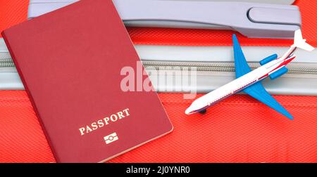 Un passeport rouge et un modèle d'avion se trouvent sur une valise rouge. Voyager dans le monde en avion. Banque D'Images