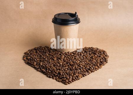 Tasse à café en papier marron à emporter avec capuchon noir sur des grains torréfiés en forme de cœur. Maquette Banque D'Images